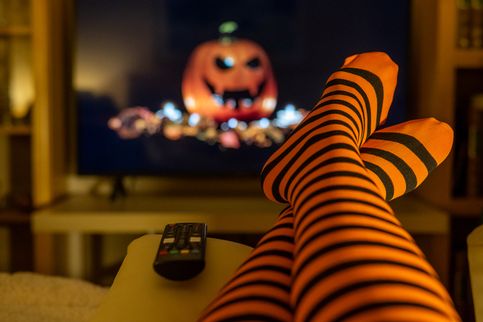 Halloween-Streaming in gemütlicher Wohnumgebung, orange gestreifte Strumpfhosen, verschwommener Fernsehbildschirm, Lifestyle drinnen und warme saisonale Vibes. 